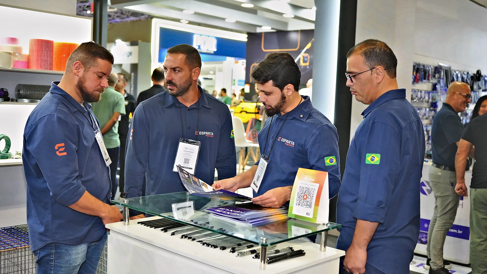Equipe da Esparta Engenharia de uniforme analisando um catálogo técnico no balcão de um expositor da feira Feicon Rio