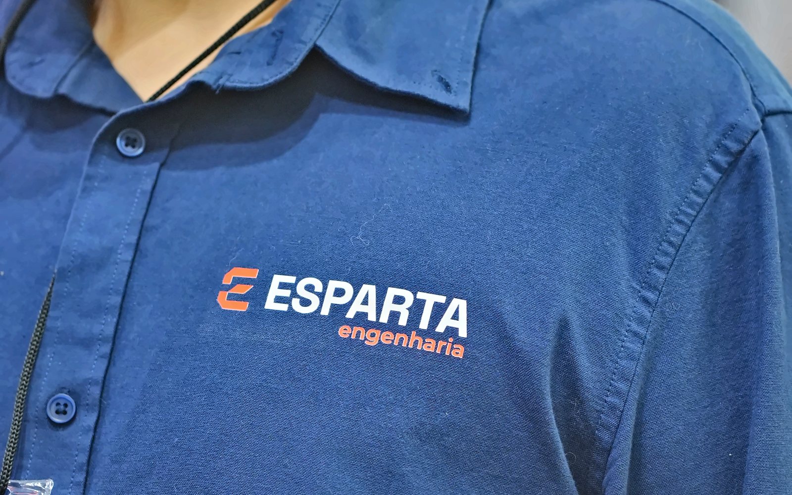 Detalhe do uniforme azul-marinho com a marca Esparta Engenharia bordada no peito
