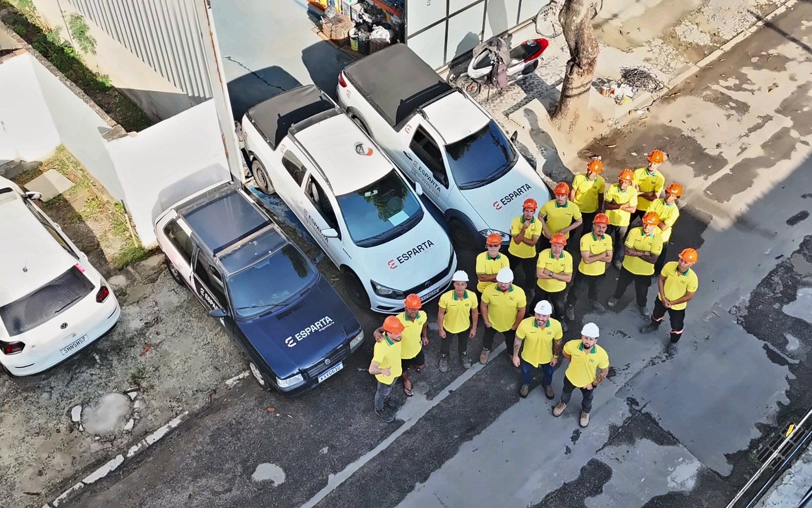 Equipe da Esparta Engenharia de camisa amarela e capacete vista de cima, ao lado das picapes da empresa